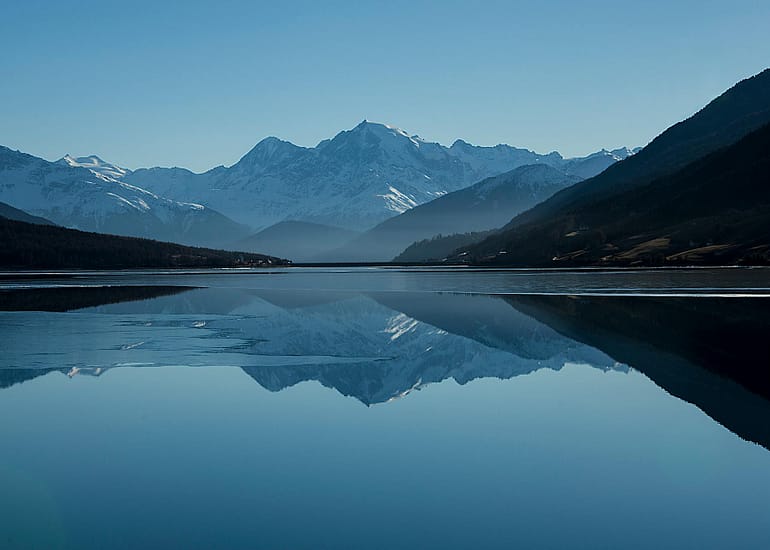Mountain lake reflecting snow-capped peaks under blue sky